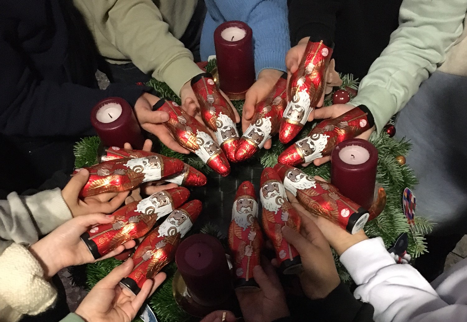 Kinder halten im Kreis um den Adventskranz faire Schokoladen-Nikoläuse in die Kamera.