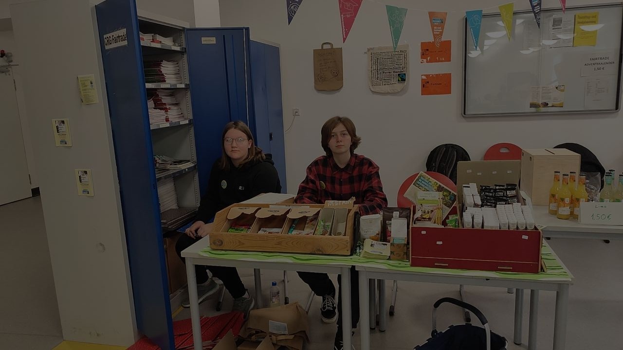 Laura und Vianna, zwei Schülerinnen der Mittelstufe, besetzen den Fairtradestand in der Mensa. Es gibt faire Süßigkeiten u. faire Limonade.