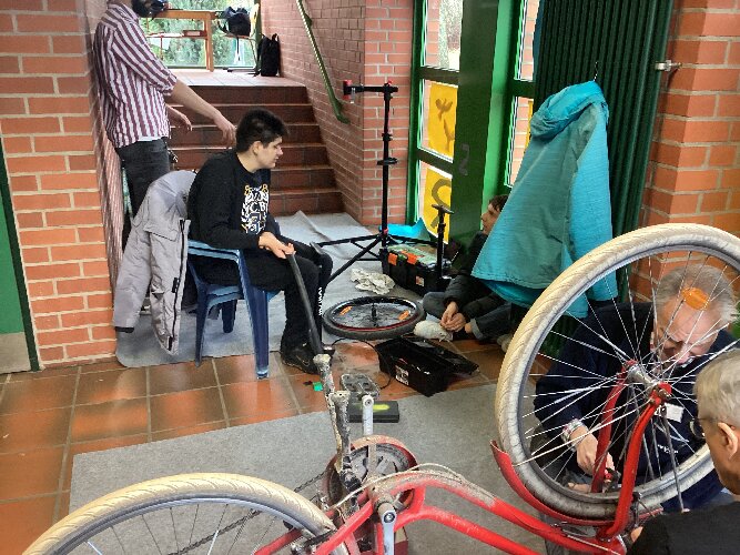 Zwei Schüler, Herr Heitmann und die ehrenamtlichen Helfer reparieren Fahrräder.