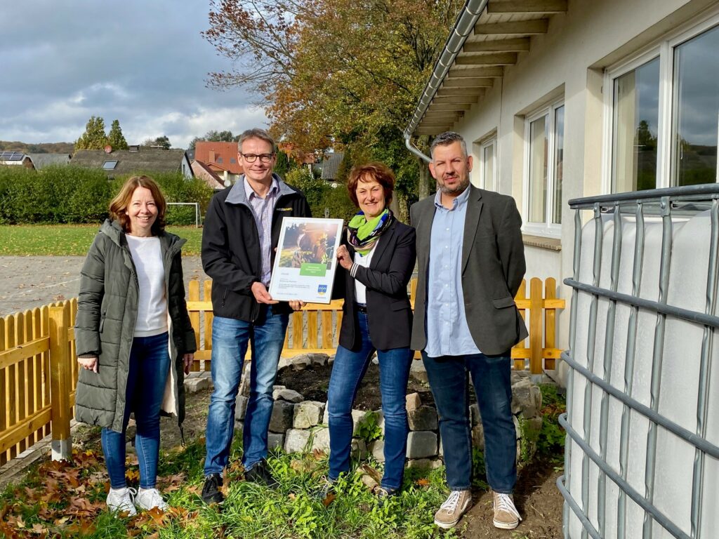 Die Schulleitung bekommt eine Urkunde im neuen Schulgarten überreicht.