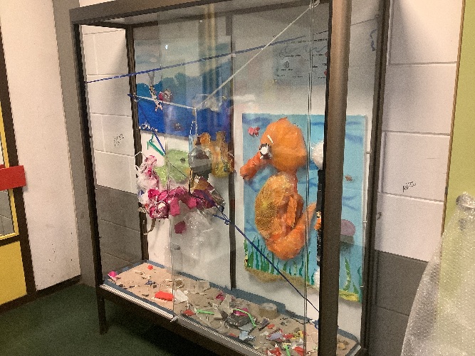 Aus verschiedenen Plastikabfällen ist ein Meer in einem Schaukasten dargestellt. Aus orangenem Abfall ist ein Seepferdchen dargestellt. Außerdem gibt es Schildkröten und Netzte in denen sie sich verfangen. 