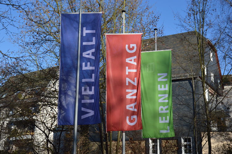 Zu sehen sind die drei Flaggen, die die Schlagworte des Schulmottos der ROS tragen: Vielfalt (blau), Ganztag (rot) und Lernen (grün).