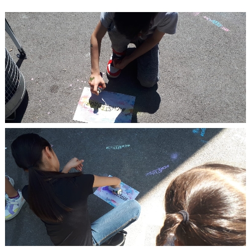 Die Kinder sprühen mit Kreidefarben den Schriftzug auf den Schulhof.
