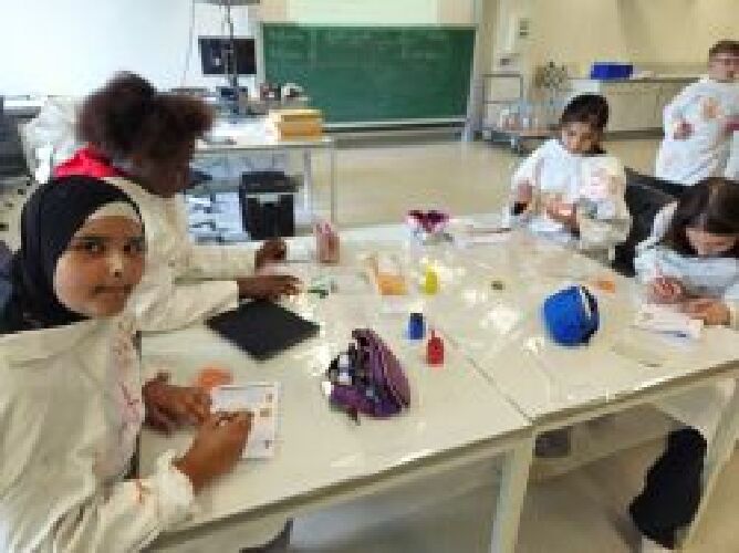SchülerInnen arbeiten mit Stiften, Heften und Farben im Lernlabor. Sie tragen weiße Malkittel.
