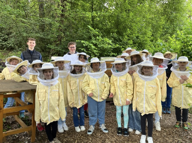 Grundschülerinnen und Grundschüler stehen in Imkerausstattung vor zwei Bienenstöcken.