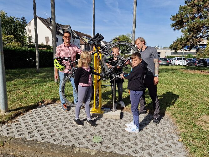 Lehrer und Schülerin und Schüler bestaunen die neue Fahrrad Station mit Fahrrad 