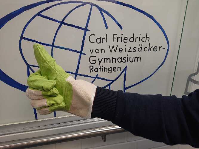 Man sieht einen Handschuh des Dreck-Weg-Tags in Ratingen vor dem Schullogo des CFvW-Gymnasiums.