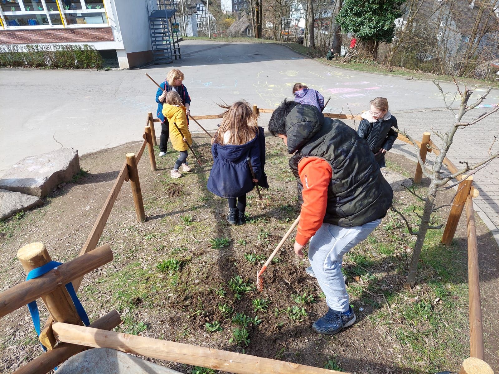 Kinder harken in einem eingezäunten Bereich des Schulhofs