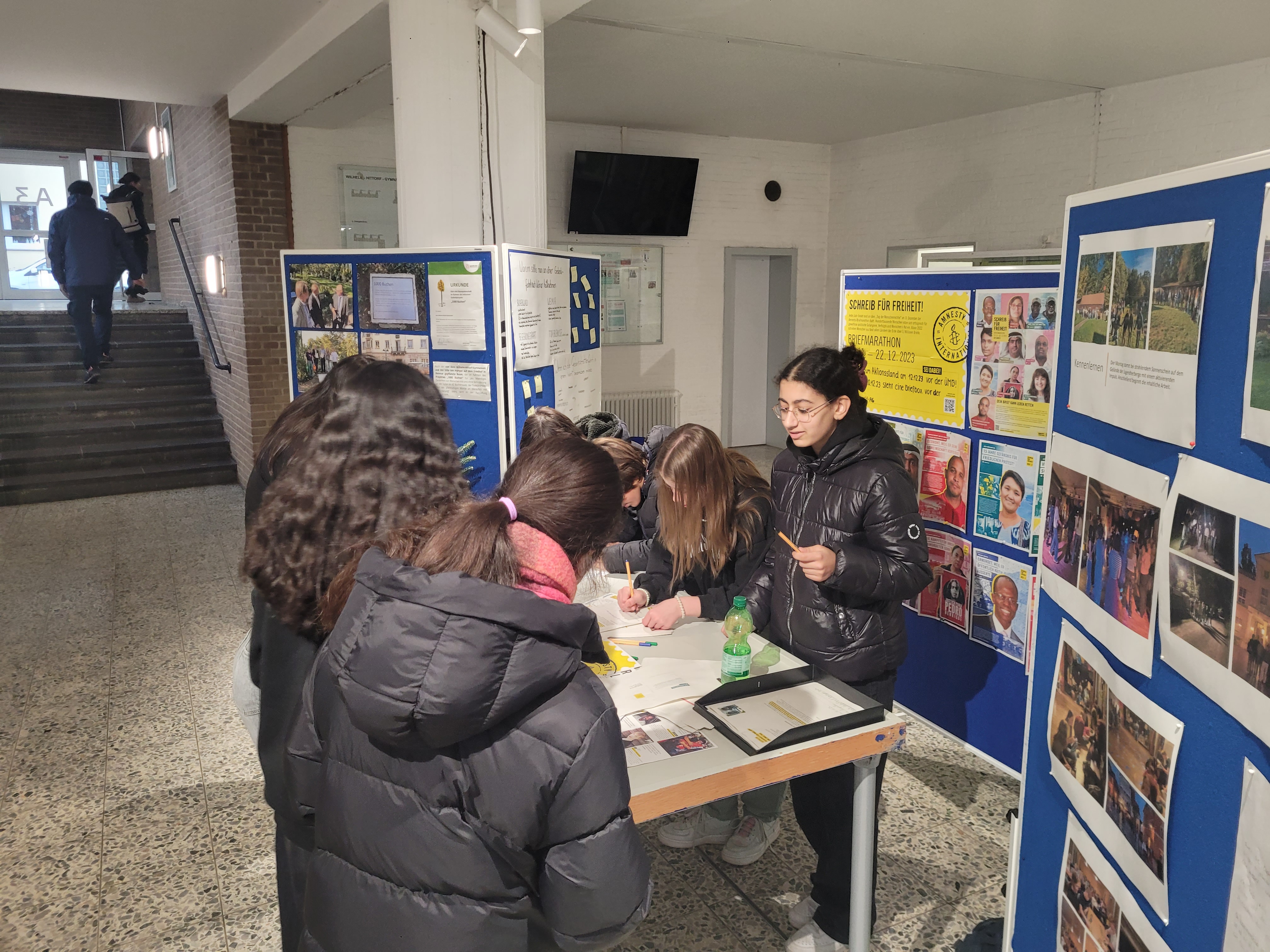 Die Schüler*innen der One-World-AG sammeln vor einer Stellwand Briefe für die Unterstützung von Menschenrechtsaktivist*innen auf der Welt