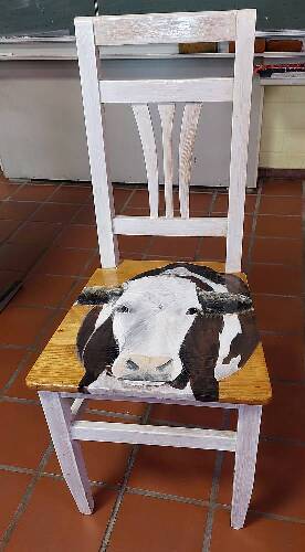 Das Bild zeigt einen alten Holzstuhl vom Sperrmüll, der durch einen nachhaltigen, weißen Farbanstrich und dem auf der Sitzfläche aufgebrachten Bild einer Kuh einen neuen Wert erhielt.  