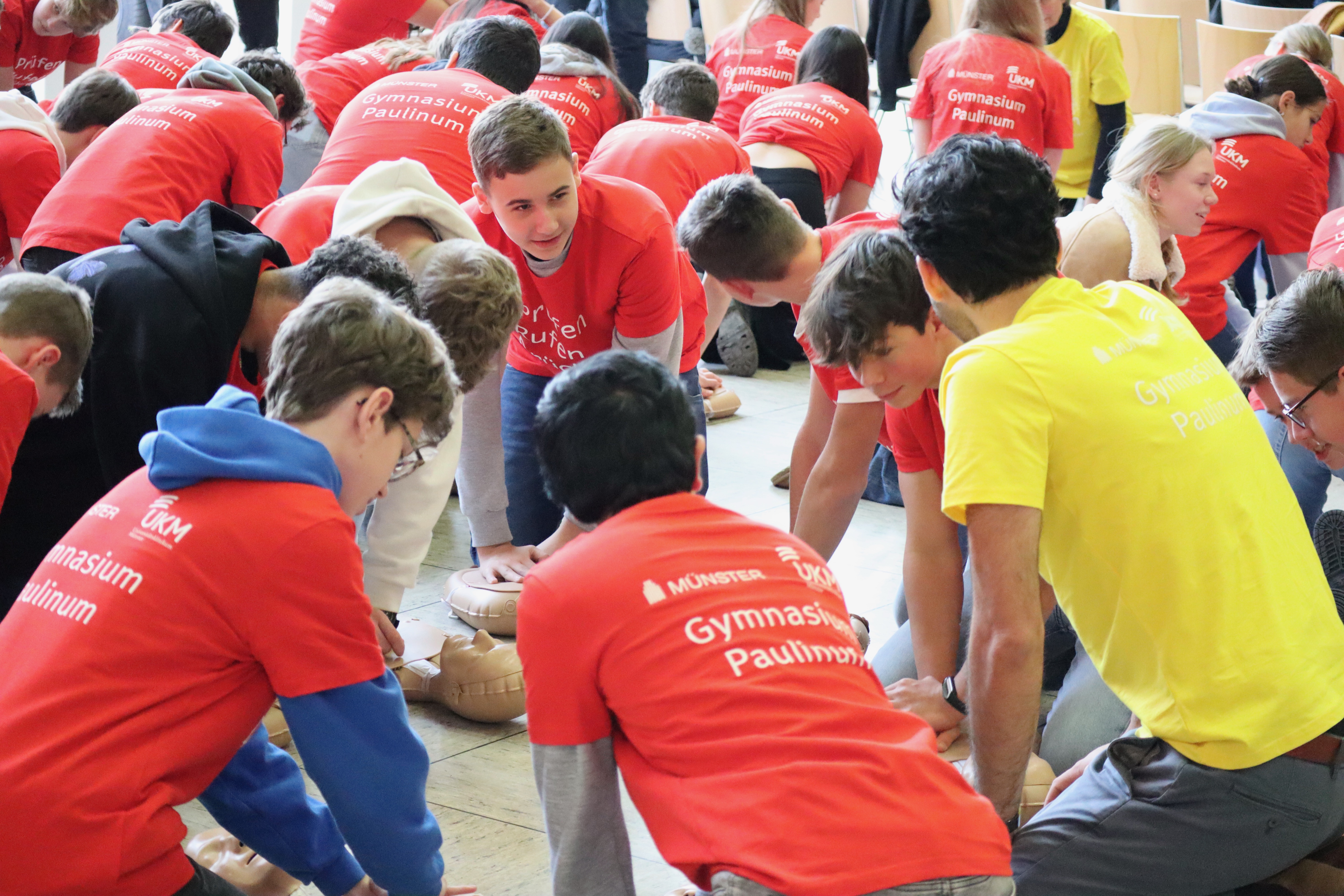 Schülerinnen und Schüler in roten T-Shirts trainieren die Reanimation an Übungspuppen